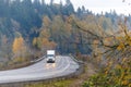 Big rig white semi truck with trailer and turned on headlight driving on the winding wet road in raining autumn weather with