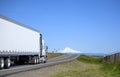 Big rig white semi truck transporting cargo in dry van semi trailer running on the narrow road with snow mountain ahead Royalty Free Stock Photo