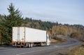 Big rig white semi truck transporting cargo in semi trailer with rusty back doors frame running on the winding road Royalty Free Stock Photo