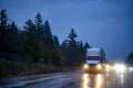 Big rig white semi truck with turned on head lights transporting cargo in semi trailer running on the night dark wet road with Royalty Free Stock Photo