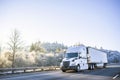 Big rig white technological semi truck with reefer semi trailer going on the winter road with frost trees on the hill Royalty Free Stock Photo