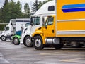 Big rigs semi trucks different makes and sizes standing in row on truck stop parking lot