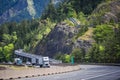 Big rigs semi trucks with different semi trailer running with another traffic cars on the winding road along the rocky mountain Royalty Free Stock Photo