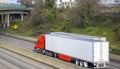 Big rigs semi trucks with dry van semi trailers running side by side on the wide divided multiline highway road with bridge at the Royalty Free Stock Photo