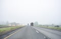 Big rigs semi trucks with semi trailers and another traffic moving on the straight divided highway road at foggy weather with bad