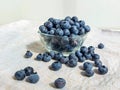 Big, ripe cultivated blueberries or highbush blueberries in a glass bowl and on table covered with gray tablecloth with white