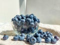 Big, ripe cultivated blueberries or highbush blueberries in a glass bowl and on table covered with gray tablecloth with white