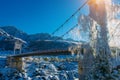 Big road bridge over frozen river against a backdrop of snow-capped mountain slopes and bright blue sky on a sunny winter day Royalty Free Stock Photo