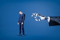 Big robotic hand ready to flick a small sad businessman on blue background Royalty Free Stock Photo