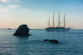 Big rock and sailing ship at sunset in front of city harbor, Skopelos island