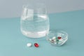 Big round glass of water, little transparent bowl with pills and capsules, one white pill ans red capsule lie near, Royalty Free Stock Photo