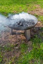 Big round grill with charcoals smoking in summer time