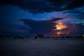 Big sandy beach and a lighthouse with lightning in the dark blue sky in the background Royalty Free Stock Photo