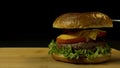 Big single cheeseburger isolated on black background. Stock footage. Close up of craft beef burger on wooden surface