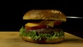 Big single cheeseburger isolated on black background. Stock footage. Close up of craft beef burger on wooden surface