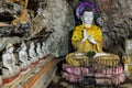 Big sitting Buddha wearing colorful neon crown, yellow clothes covering the shoulders. Statues inside a sacred limestone cave. Hpa