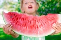 Little girl in green dress, barefoot standing in the park with big slice watermelon. Royalty Free Stock Photo