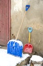 Big and small father and child snow shovels near wall