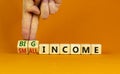 Big or small income symbol. Businessman turns wooden cubes and changes words Small income to Big income. Beautiful orange table