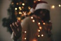 Big sparkler burning in hand of stylish hipster girl in santa hat on background of modern christmas tree light in dark room. Happy Royalty Free Stock Photo