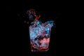 Big splash in a rocks glass under blue and orange lights isolated on a black background Royalty Free Stock Photo