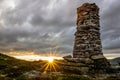 Big stone cairn outdoors in the wilderness during sunset with big sunburst Royalty Free Stock Photo