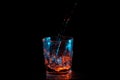 Big stream of water being poured into a square glass under blue and orange lights isolated on a black background Royalty Free Stock Photo