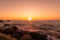 Big sun on skyline at sunset. Ocean water splash on rock beach with beautiful sunset sky and orange clouds. Sea wave splashing on Royalty Free Stock Photo