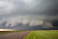 A big supercell storm with a shelf cloud and a wall cloud looms over a road.