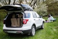 Big SUV car with open trunk and roof rack box against happy young family having fun and enjoying outdoor on picnic blanket at Royalty Free Stock Photo