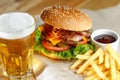 Big tasty burger and fries with beer on foreground on the wooden table Royalty Free Stock Photo