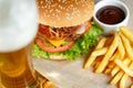 Big tasty burger and fries with beer on foreground on the wooden table Royalty Free Stock Photo