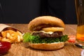 Big tasty burger on the wooden table with becon and french fries. Delicious dinner with cheese, tomatoos and salad. Fast food with