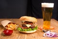 Big tasty burger on the wooden table with becon and french fries. Delicious dinner with cheese, tomatoos and salad. Fast food with