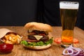 Big tasty burger on the wooden table with becon and french fries. Delicious dinner with cheese, tomatoos and salad. Fast food with