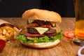 Big tasty burger on the wooden table with becon and french fries. Delicious dinner with cheese, tomatoos and salad. Fast food with