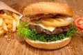 Big tasty burger on the wooden table with becon and french fries. Delicious dinner with cheese, tomatoos and salad. Fast food with
