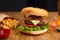 Big tasty burger on the wooden table with becon and french fries. Delicious dinner with cheese, tomatoos and salad. Fast food with