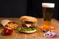 Big tasty burger on the wooden table with becon and french fries. Delicious dinner with cheese, tomatoos and salad. Fast food with