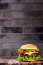 Big tasty classic hamburger on wooden table and brick wall on background