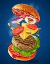 Big tasty home made burger with flying ingredients on blue background. Food levitation concept