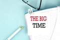 THE BIG TIME text on a sticky on notebook with pen and glasses , blue background