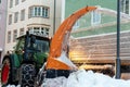 Big tractor with chains on wheel blowing snow from city street into dump truck body. Cleaning streets and snow removal after Royalty Free Stock Photo