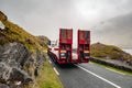 Big truck with empty red trailer for heavy machinery on a narrow road in a mountains. Low cloudy sky
