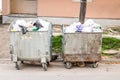 Big two metal dumpster garbage can full of overflow litter polluting the street in the city