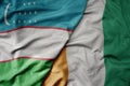 big waving national colorful flag of cote divoire and national flag of uzbekistan