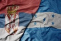 big waving national colorful flag of serbia and national flag of honduras