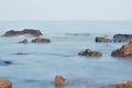 Big wet boulders in shore in smooth wavy sea. Stony coast defies to waves of Baltic Sea  clear horizon sky with blurred Sun in Royalty Free Stock Photo