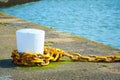 Big white bollard on the stone pier with yellow metal chain for ships. Royalty Free Stock Photo