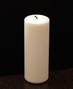 Big white candle isolated on black, standing on wooden table. Royalty Free Stock Photo